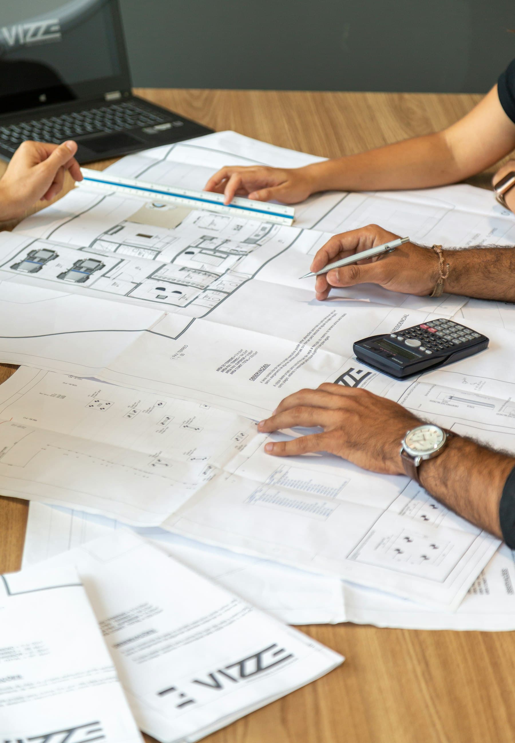 A working session around architectural plans, measuring tools, and a calculator.